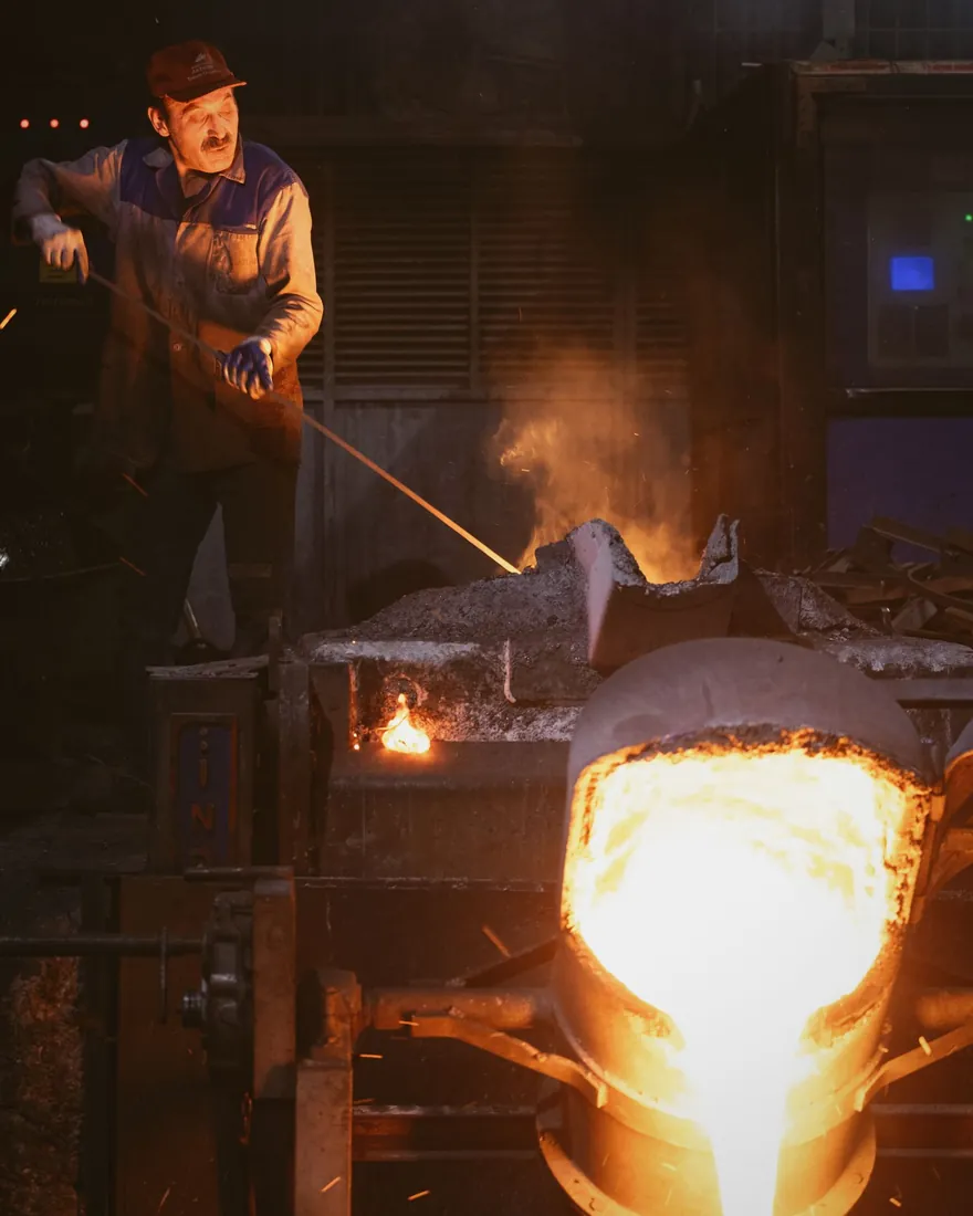 Vertido de metal fundido desde una cuchara hacia un molde en el suelo de un taller de fundición